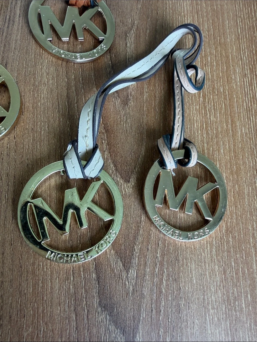 Set of four Michael Kors MK logo handbag charms featuring large round gold-tone